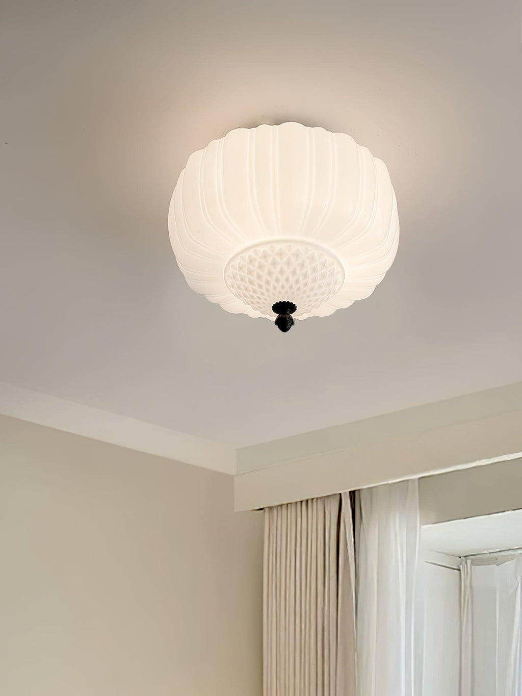 Ribbed white glass ceiling light from Clérachic on a cream ceiling, with a window and soft curtains beside it.