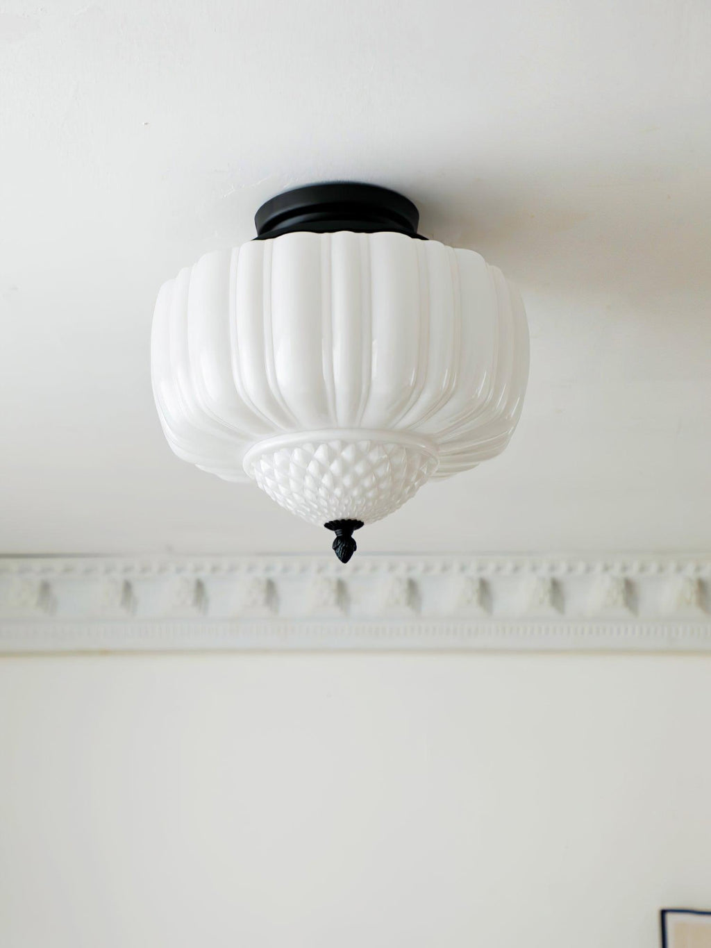 Black-canopy ceiling light from Clérachic with a ribbed white glass shade, seen from below above a plaster cornice.