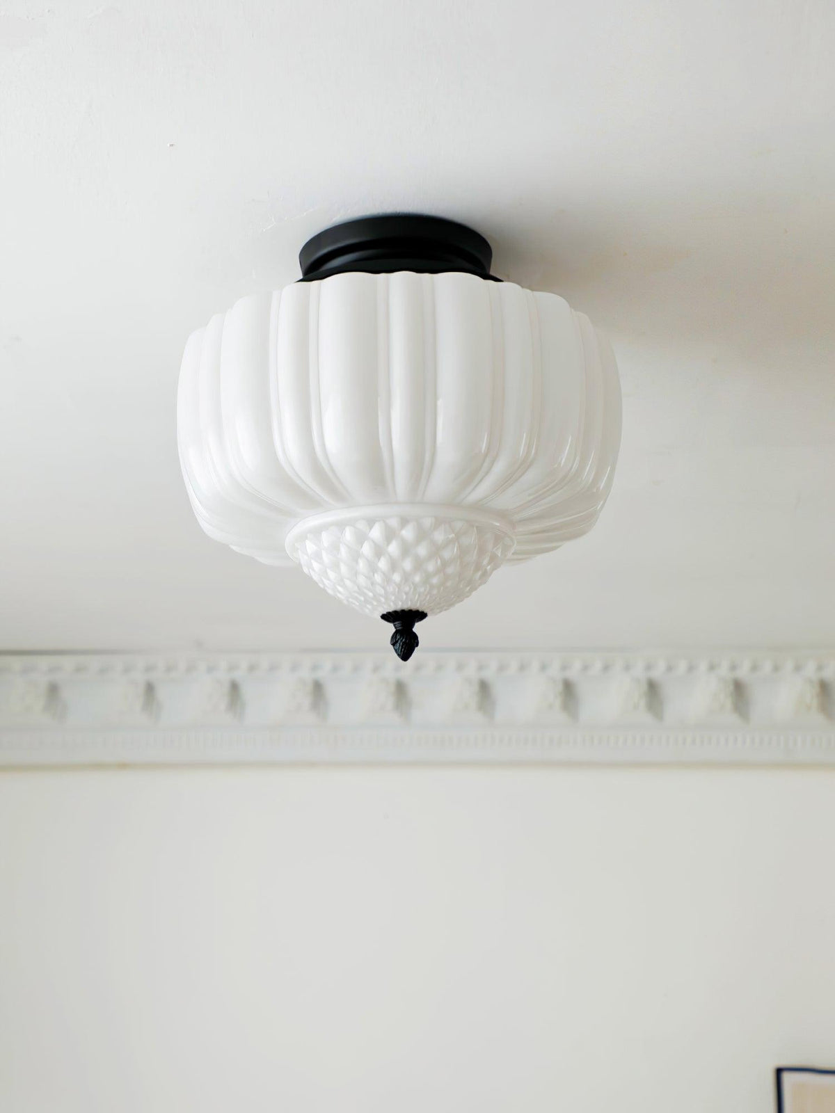Black-canopy ceiling light from Clérachic with a ribbed white glass shade, seen from below above a plaster cornice.