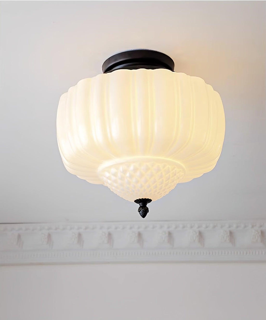 Lit ribbed milk glass ceiling light from Clérachic with a quilted lower bowl, glowing warm above a decorative cornice.