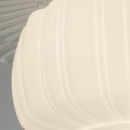 Side close view of the ribbed edge of this Clérachic ceiling light's glass shade, glowing a creamy white.