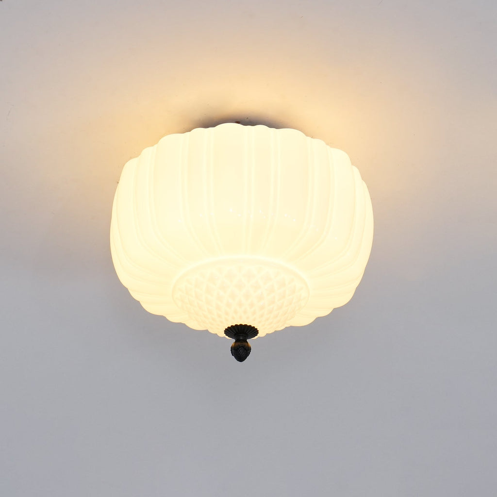 Lit Clérachic ceiling light with a ribbed milk glass shade glowing a warm yellow, casting a soft halo on the ceiling.