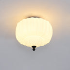 Lit Clérachic ceiling light with a ribbed milk glass shade glowing a warm yellow, casting a soft halo on the ceiling.