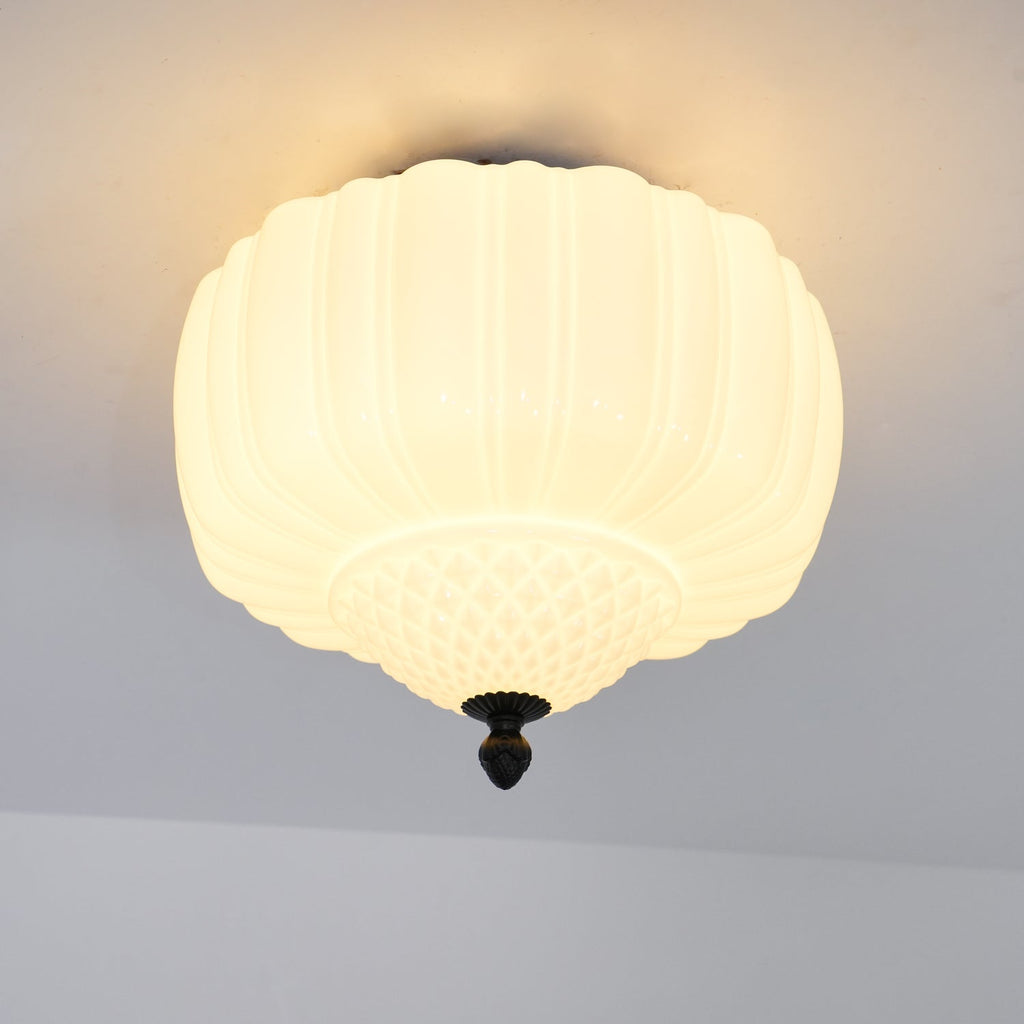 Close, lit view of the ribbed glass shade on this Clérachic ceiling light, with a warm glow spreading across the ceiling.