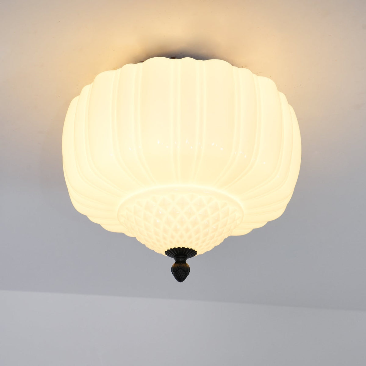 Close, lit view of the ribbed glass shade on this Clérachic ceiling light, with a warm glow spreading across the ceiling.