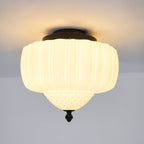 Lit white glass ceiling light from Clérachic with a black canopy, seen from below with its quilted bowl and finial.