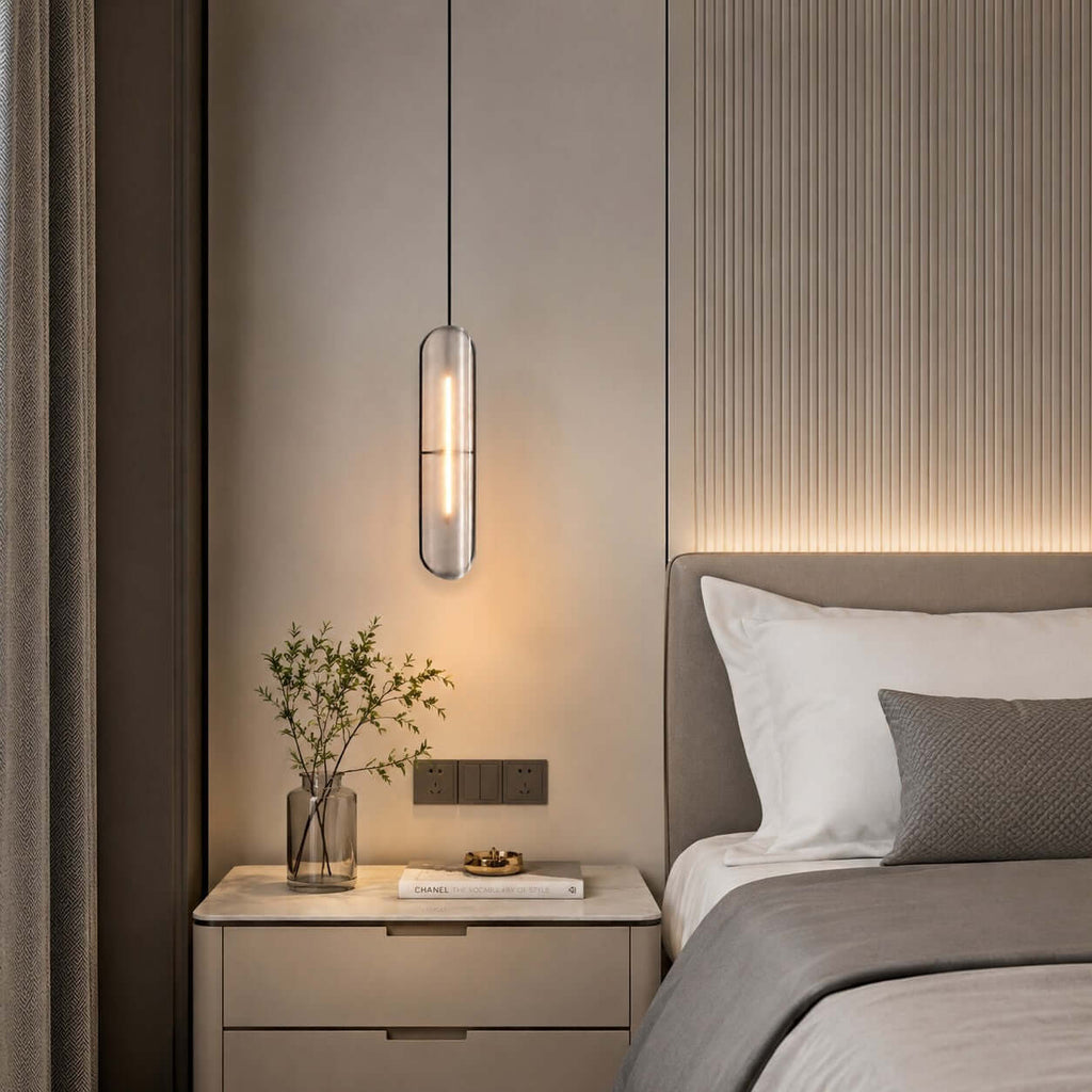 Close view of a lit Clérachic capsule pendant hanging beside a ribbed wall panel, above a cream bedside table and a plant.
