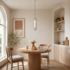 Clérachic capsule pendant hung low over a round wood dining table, in front of an arched window and a built-in shelf.
