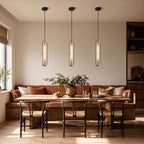 Three Clérachic capsule pendants in a row above a dining table with wishbone chairs and a rust-coloured banquette.