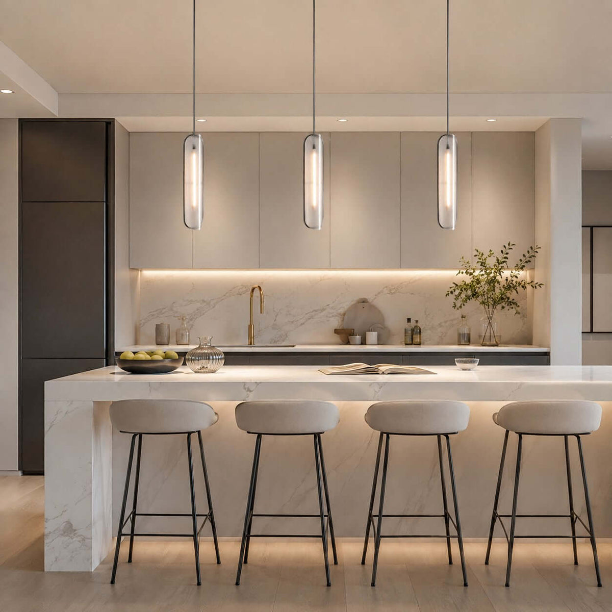 Row of three Clérachic capsule pendants lit above a marble kitchen island with four slim bar stools and under-cabinet lighting.