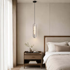 This Clérachic capsule pendant hangs by a bed with a wooden headboard, beside a bedside chest, a plant and sheer curtains.