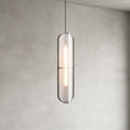 Close view of a Clérachic capsule pendant with a textured grey shade and a lit strip inside, against a plastered wall.