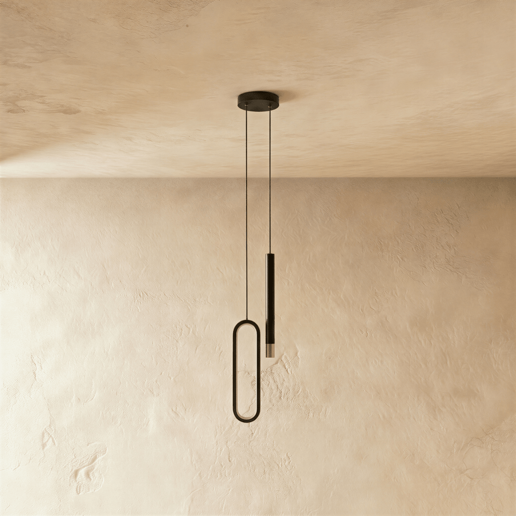 Seen from another angle, the black pendant's oval acrylic ring and rod head hang side by side against a plaster wall, Clérachic hero shot.