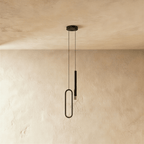 Seen from another angle, the black pendant's oval acrylic ring and rod head hang side by side against a plaster wall, Clérachic hero shot.