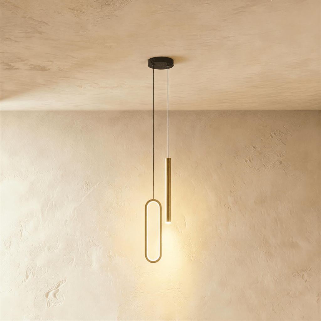 A brass-toned version of the pendant shows the same oval ring and rod pairing, both glowing warm in this Clérachic hero shot.