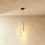 A brass-toned version of the pendant shows the same oval ring and rod pairing, both glowing warm in this Clérachic hero shot.
