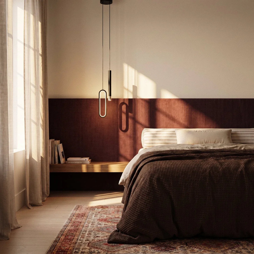 The black pendant hangs bedside over a walnut headboard and books, its oval ring glowing warm beside a made bed, Clérachic lifestyle shot.