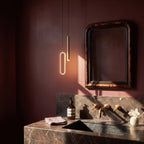 In a dark powder room, the brass pendant hangs beside an antique mirror above a marble vanity, Clérachic lifestyle shot.