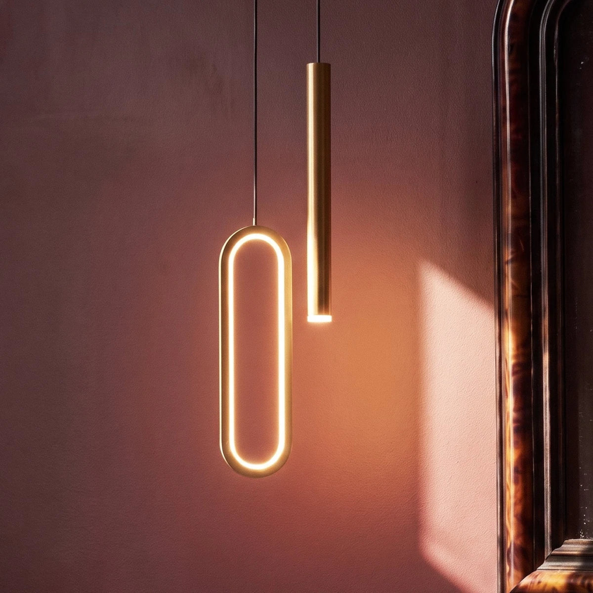 A tight crop on the brass pendant's glowing oval ring and rod head against a warm-lit wall, Clérachic detail shot.