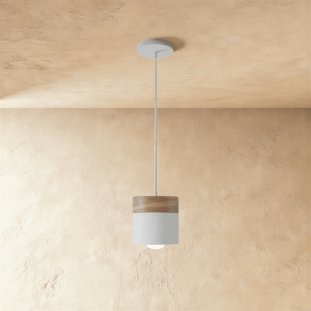 Clérachic pendant light with a walnut wood cap and white cylindrical shade, hung on a slim cord from the ceiling.