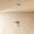 Clérachic pendant light with a walnut wood cap and white cylindrical shade, hung on a slim cord from the ceiling.