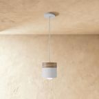 Clérachic pendant light with a walnut wood cap and white cylindrical shade, hung on a slim cord from the ceiling.