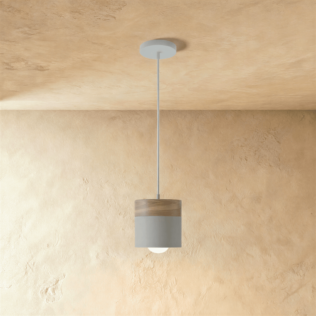 Clérachic pendant light with a wood top and grey cylinder shade, suspended on a white cord against a plaster wall.