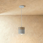 Clérachic pendant light with a wood top and grey cylinder shade, suspended on a white cord against a plaster wall.