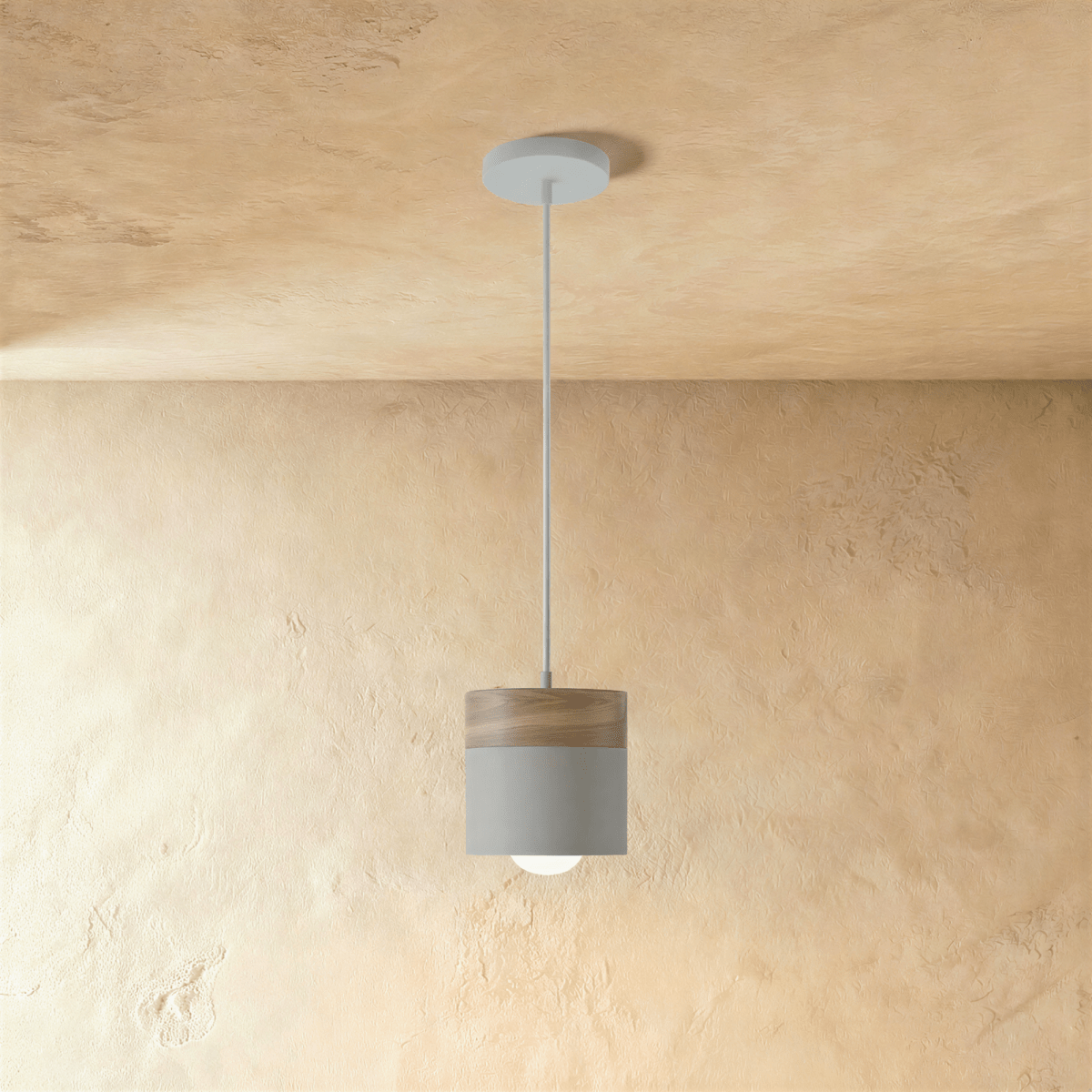 Clérachic pendant light with a wood top and grey cylinder shade, suspended on a white cord against a plaster wall.