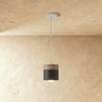 Clérachic black pendant light with a walnut wood cap, its cylindrical shade glowing warm on a slim ceiling cord.