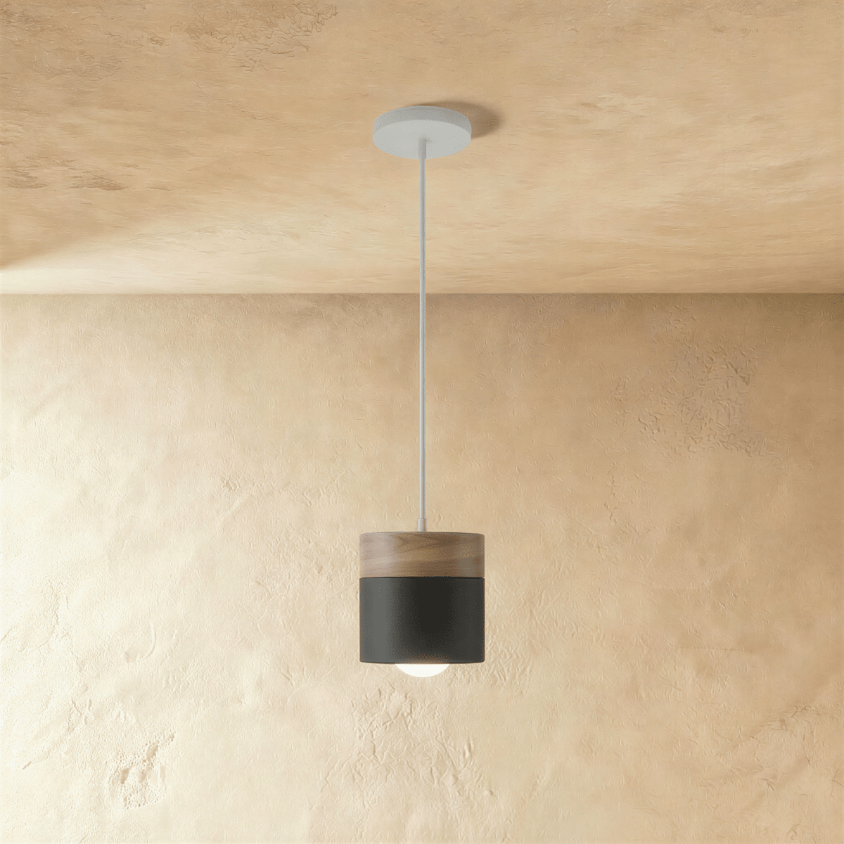 Clérachic black pendant light with a walnut wood cap, its cylindrical shade glowing warm on a slim ceiling cord.