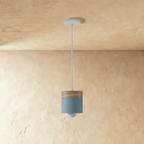 Clérachic pendant light with a dark blue cylinder shade and wood top, hung low on a cord against a plaster wall.