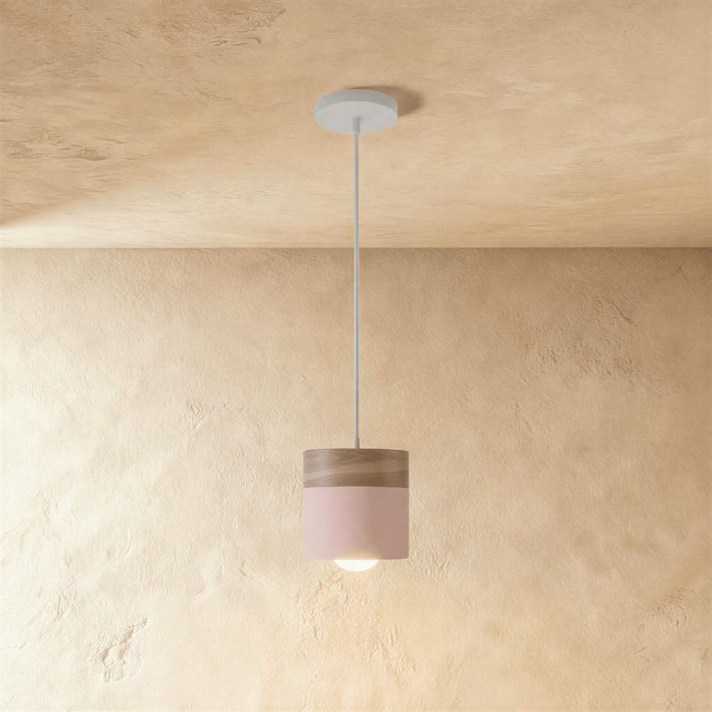 Clérachic pink pendant light with a walnut wood cap, its cylindrical shade hung low against a plaster wall.