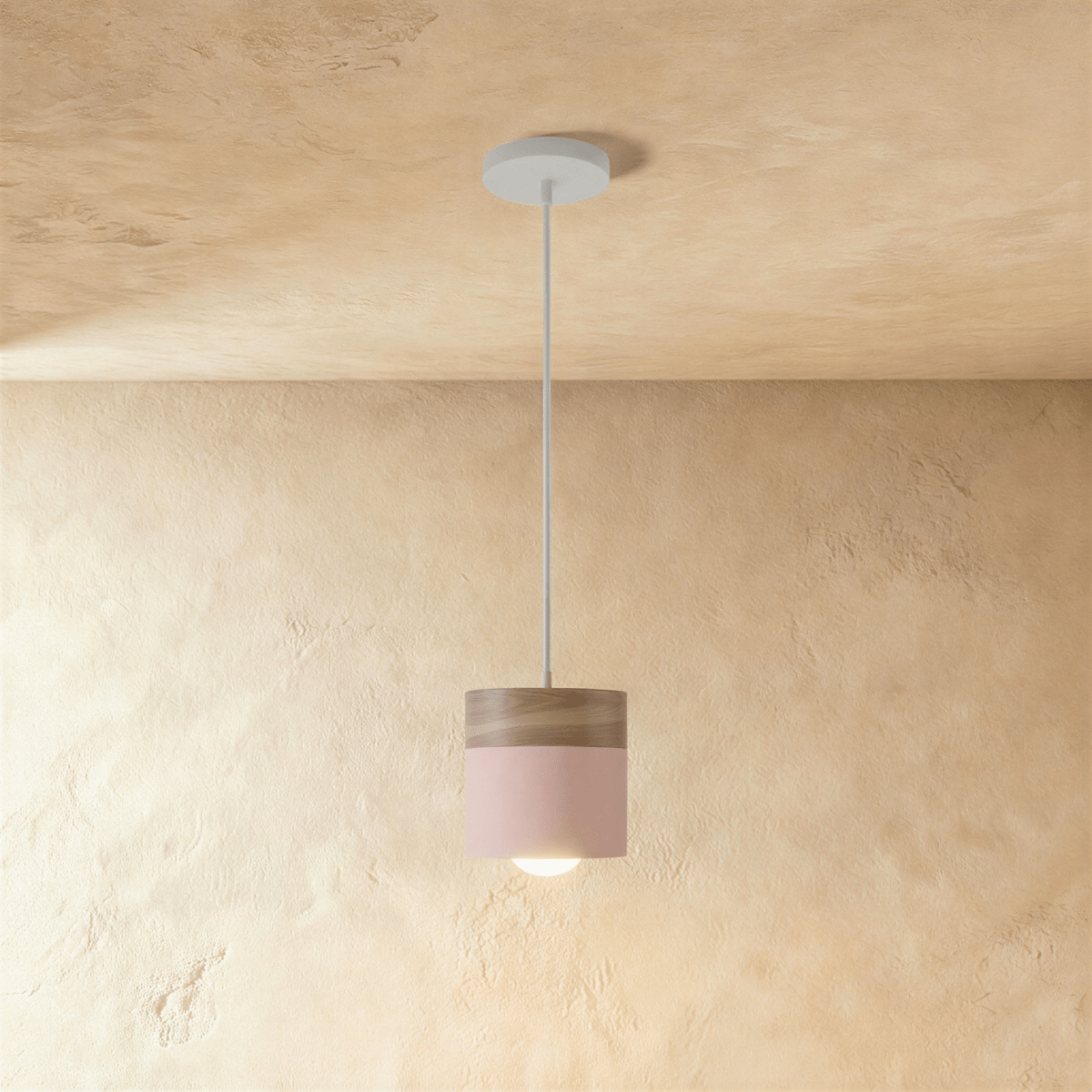 Clérachic pink pendant light with a walnut wood cap, its cylindrical shade hung low against a plaster wall.