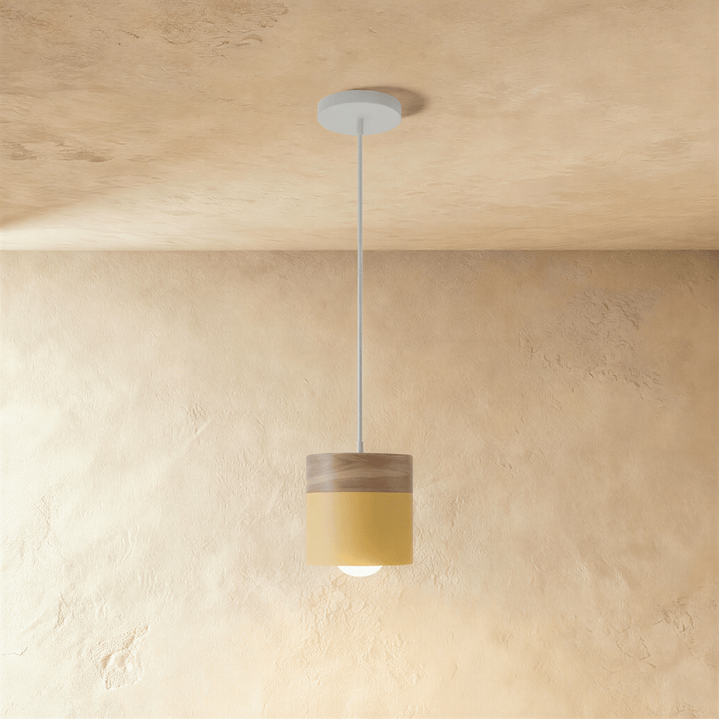 Clérachic mustard yellow pendant light with a wood top, its cylinder shade glowing warm on a white ceiling cord.