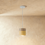 Clérachic mustard yellow pendant light with a wood top, its cylinder shade glowing warm on a white ceiling cord.