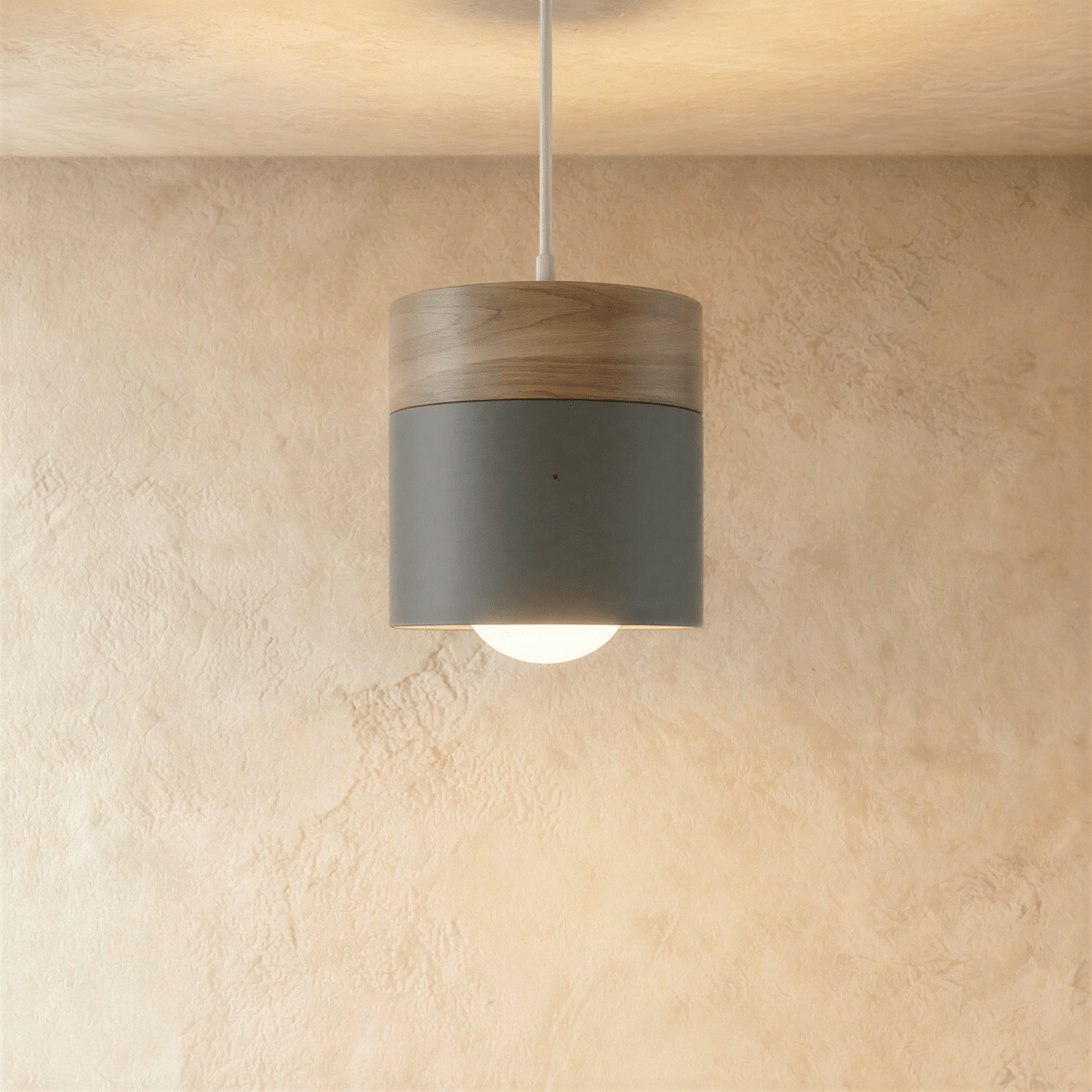 Clérachic pendant light shown close, its wood cap and grey cylinder shade glowing warm around the bulb.
