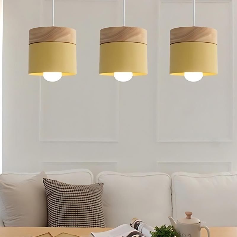 Clérachic mustard yellow pendant lights, three hung in a row above a cream sofa against a panelled white wall.