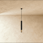 Clérachic black cylinder pendant light, gold rim glowing at its tip, suspended against a textured plaster wall.