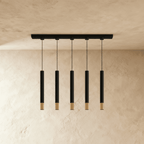 Clérachic linear five-pendant fixture, black cylinders with gold rims, shown against a warm plaster backdrop.