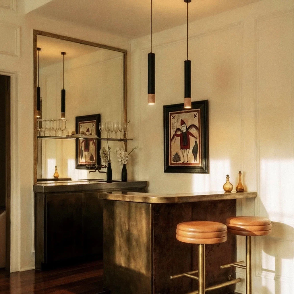 Clérachic black pendant lights with gold rim tips hang over a home bar counter beneath a large brass mirror.