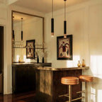 Clérachic black pendant lights with gold rim tips hang over a home bar counter beneath a large brass mirror.