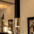 Clérachic close-up shows the black pendant's gold rim tip glowing warm, framed art blurred in the background.