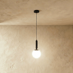 Clérachic black metal pendant light with a milk-glass globe shade, hanging from a slender cord against a plaster wall.