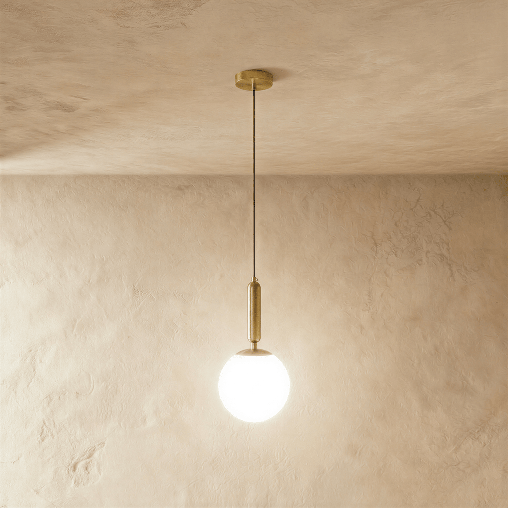 Clérachic brass pendant light with a milk-glass globe shade, hanging from a slender cord against a plaster wall.