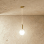 Clérachic brass pendant light with a glowing white globe shade, suspended from a round brass ceiling canopy.