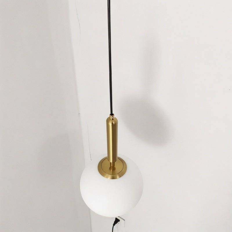 Clérachic brass pendant light in close detail, showing the fluted brass socket housing above a white globe shade.