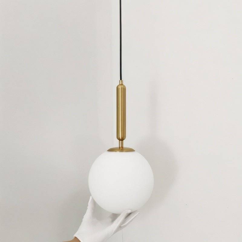 Clérachic brass pendant light in close detail, a gloved hand cradling the smooth white glass globe shade.