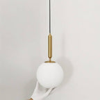 Clérachic brass pendant light in close detail, a gloved hand cradling the smooth white glass globe shade.
