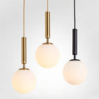 Clérachic globe pendant lights in brass and black finishes grouped together, each with a glowing white glass shade.